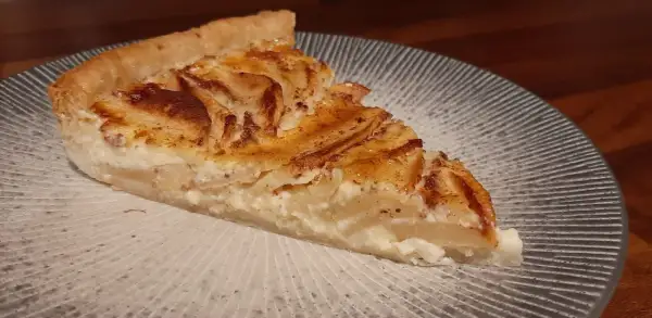 Une part de tarte aux pommes à l'ancienne, avec sa garniture crémeuse et ses pommes caramélisées, sur une assiette décorée.