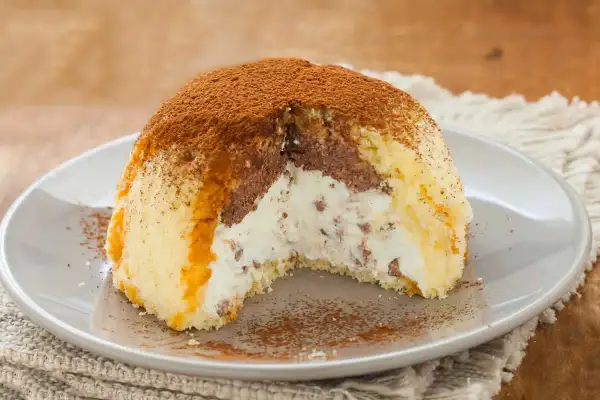 Gâteau glacé en forme de dôme, garni de crème et de chocolat, saupoudré de cacao. Parfait pour une recette génoise.