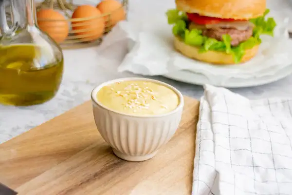 Sauce burger maison crémeuse, garnie de flocons, prête à accompagner un burger savoureux. Huile d'olive et œufs en arrière-plan.