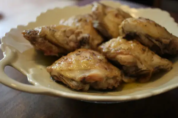 Plusieurs hauts de cuisse de poulet au four, dorés et assaisonnés d'herbes, reposent sur une assiette blanche festonnée.