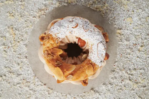 Un délicieux Paris-Brest, saupoudré de sucre glace et garni d'amandes grillées, attend d'être dégusté.