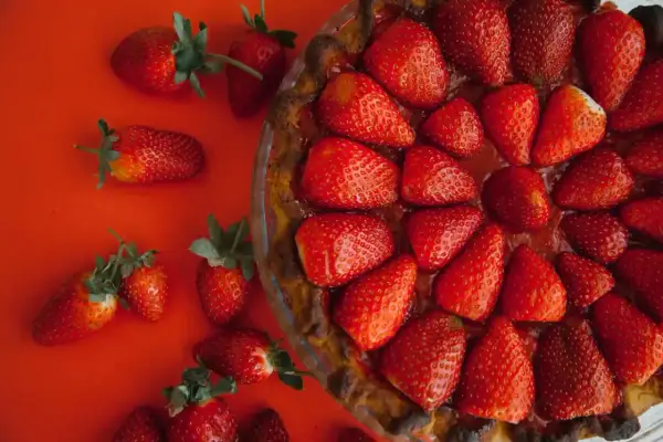 Tarte aux fraises sans crème pâtissière, garnie de fruits rouges frais sur fond rouge. Un délice simple et fruité.