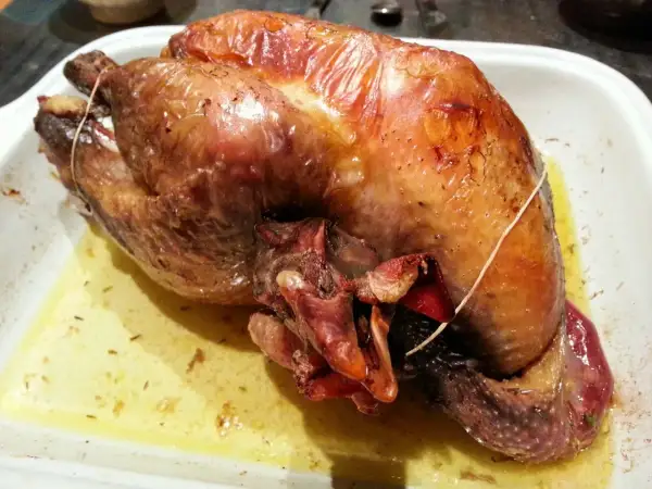 Une pintade au four, dorée et juteuse, repose dans un plat blanc, baignant dans son jus savoureux.