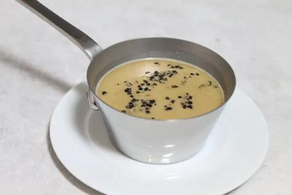 Sauce au poivre recette de chef, onctueuse et garnie de grains de poivre concassés, servie dans une petite casserole en métal sur une assiette blanche.