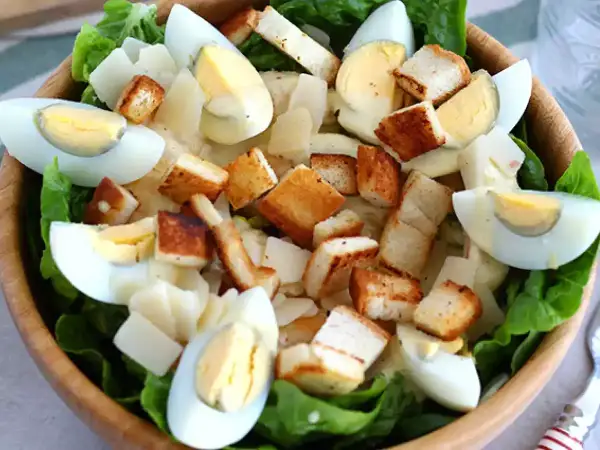 Salade César appétissante dans un bol en bois, garnie d'œufs durs, de croûtons dorés et d'une onctueuse sauce César.