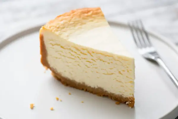 Une part de gâteau au fromage blanc onctueux, digne d'un gâteau au fromage blanc Cyril Lignac, sur une assiette blanche avec une fourchette.