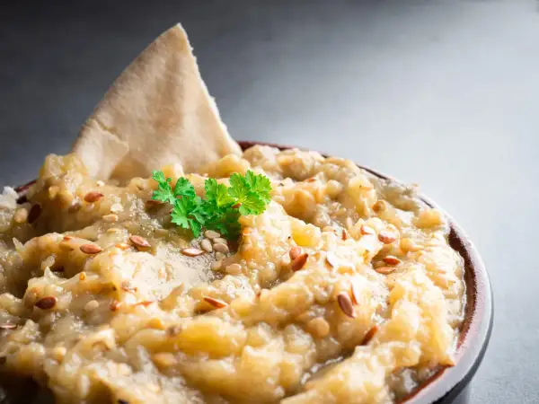 Un bol de le vrai caviar d'aubergine, garni de persil frais et de graines de sésame, avec un morceau de pain pita.