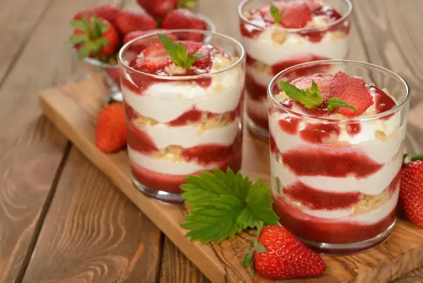 Délicieux tiramisu fraise en verrines, alternant couches de crème, biscuits émiettés et coulis de fraises, garni de fruits frais et de menthe.