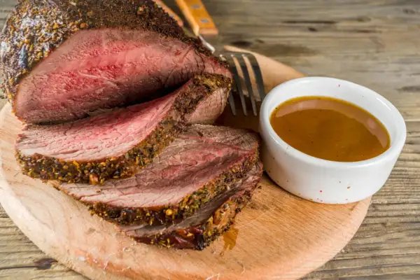 Un délicieux roti de boeuf basse température, tranché et servi avec une sauce savoureuse sur une planche en bois.