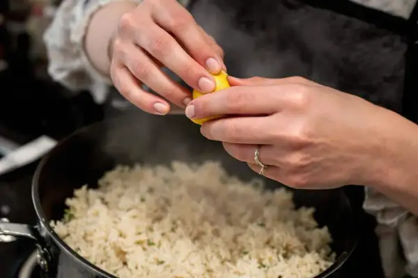 Cuisson du riz rouge : une main presse un quartier de citron sur le riz fumant dans une casserole.